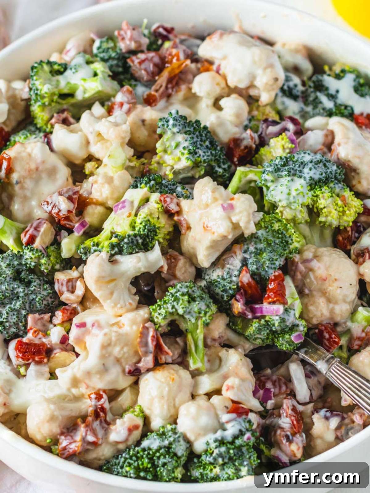 Creamy Broccoli Cauliflower Salad with Tangy Greek Yogurt 2 Healthy broccoli cauliflower salad with Greek yogurt dressing close up in a white bowl, garnished with fresh herbs.