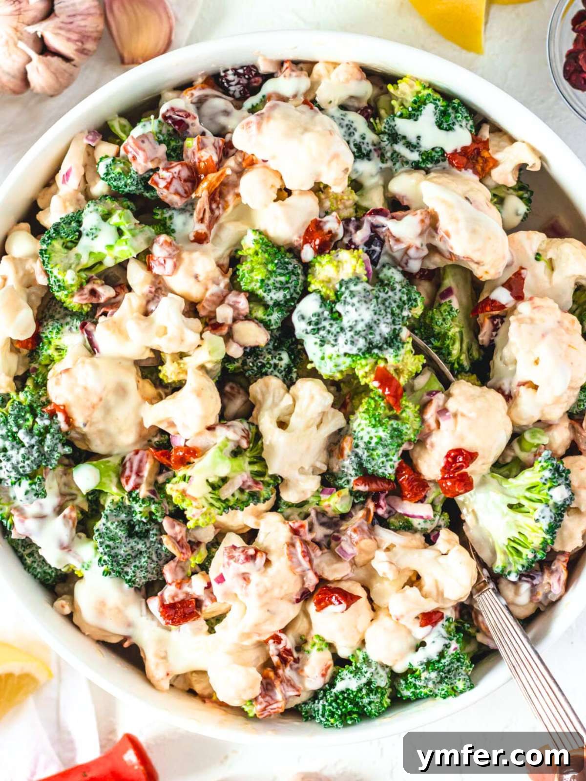 Creamy Broccoli Cauliflower Salad with Tangy Greek Yogurt 3 Overhead view of creamy healthy broccoli cauliflower salad with sun-dried tomatoes and cranberries in a large serving bowl.