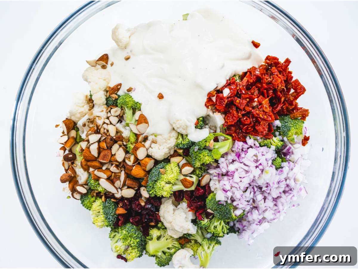 Creamy Broccoli Cauliflower Salad with Tangy Greek Yogurt 7 Step 3 Adding chopped red onion, toasted almonds, dried cranberries, and sun-dried tomatoes to the broccoli and cauliflower salad base.
