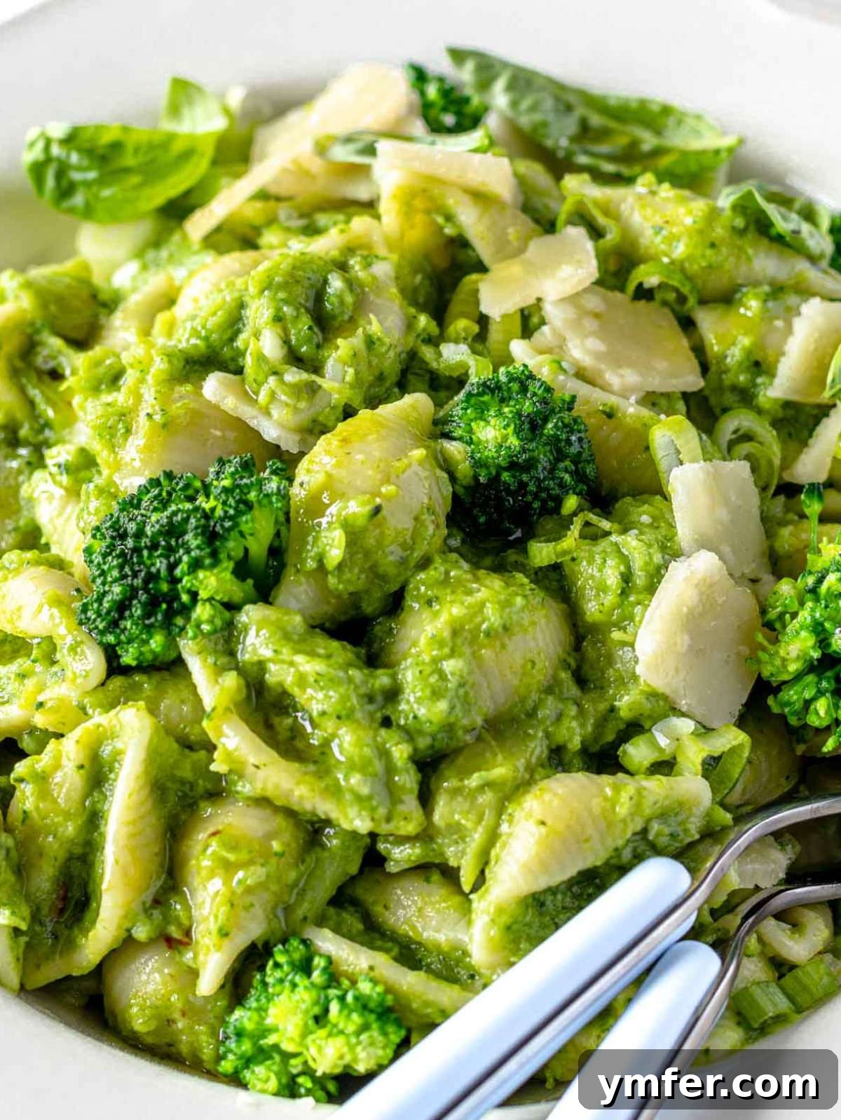 Close up of creamy smashed broccoli pasta topped with parmesan and basil.