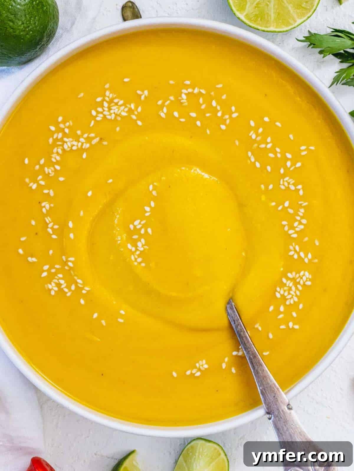 Nourishing Creamy Coconut Pumpkin Soup for Fall 4 Top down view of creamy coconut pumpkin soup garnished with vibrant lime wedges and fresh cilantro leaves, ready to be enjoyed.