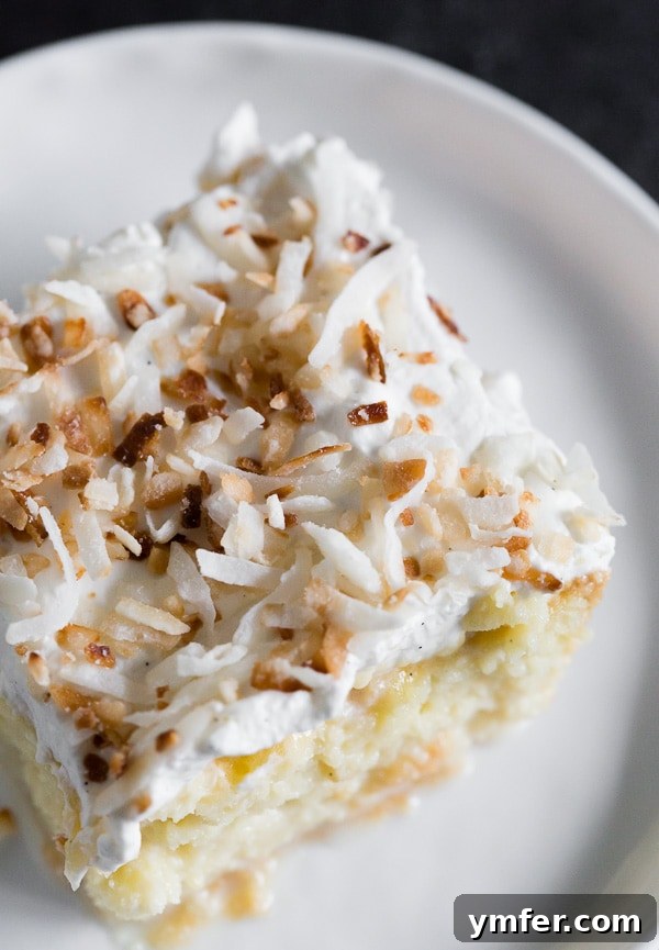 Coconut Cloud Tres Leches 4 A slice of Toasted Coconut Tres Leches Cake on a white plate, highlighting its moist interior and generous toasted coconut garnish.