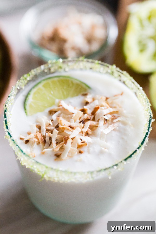 Tropical Coconut Lime Margarita Frost 3 A close-up of a coconut lime frozen margarita, artfully rimmed with lime sugar, highlighting its appealing texture and garnish.