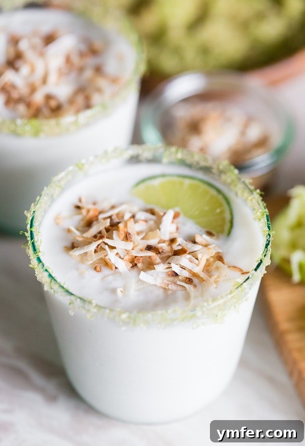 Tropical Coconut Lime Margarita Frost 5 A perfectly blended coconut lime frozen margarita, garnished with toasted coconut and a lime wheel, presenting a delightful and refreshing appearance.