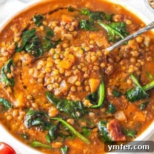 Warm bowl of spinach lentil soup with olive oil drizzle and lemon wedge, ready to be enjoyed.