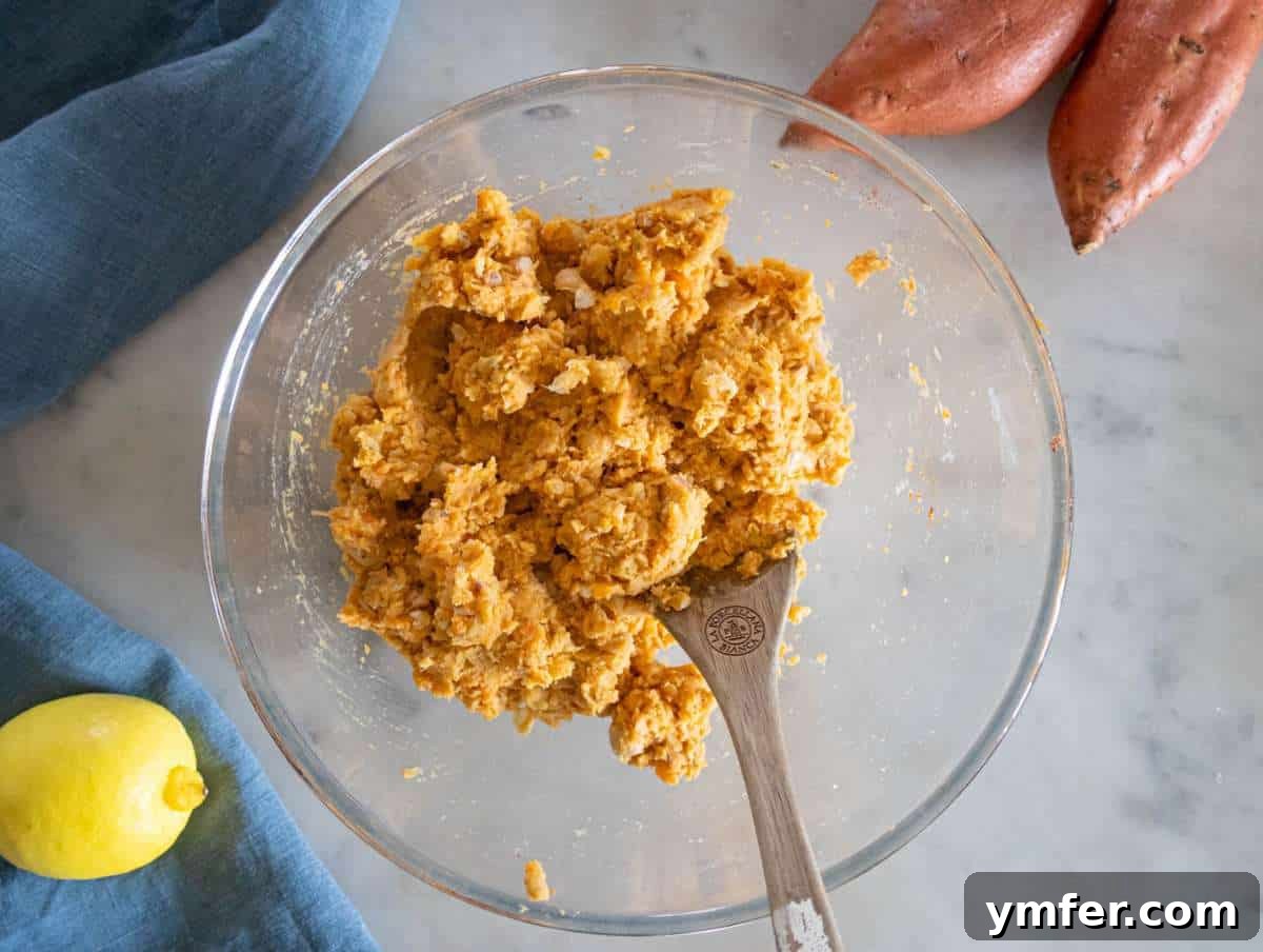 Simple Wholesome Chickpea Sweet Potato Patties 6 Step 2 – Finely chopped onion, grated garlic, parmesan cheese, and a blend of aromatic spices are being added to the mashed chickpea sweet potato base.