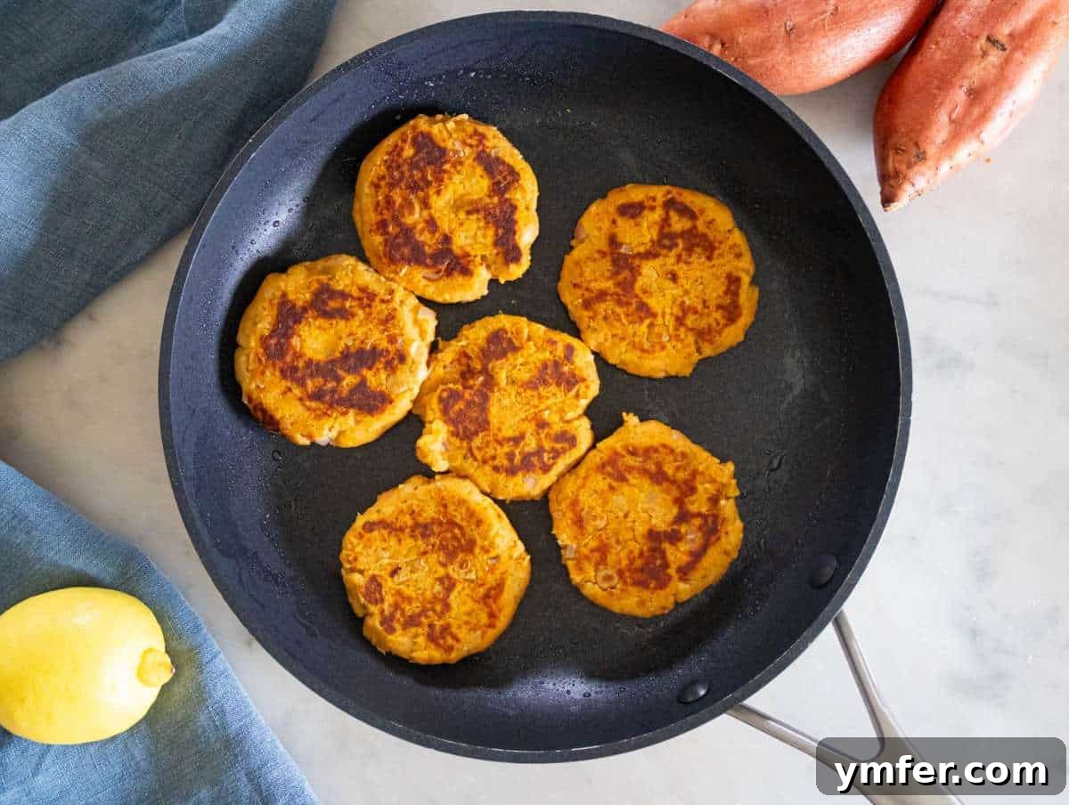 Simple Wholesome Chickpea Sweet Potato Patties 7 Step 3 – Several chickpea sweet potato patties are sizzling in a nonstick skillet, achieving a perfect golden-brown and crispy finish on both sides.