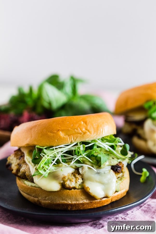 Sweet & Savory Cranberry Pesto Chicken Burgers 2 Flavorful cranberry pesto chicken burgers topped with melted brie, fresh microgreens, and a creamy pesto mayonnaise, served on a toasted bun.