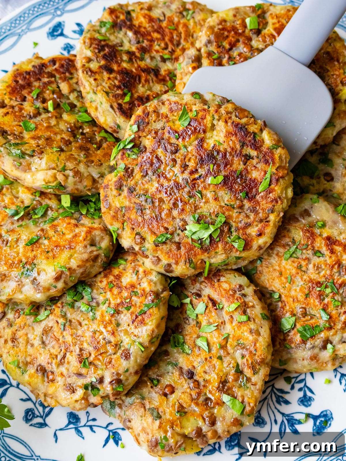 Close up picture of crispy golden-brown lentil potato patties stacked on a plate with fresh herbs for garnish, ready to be served.
