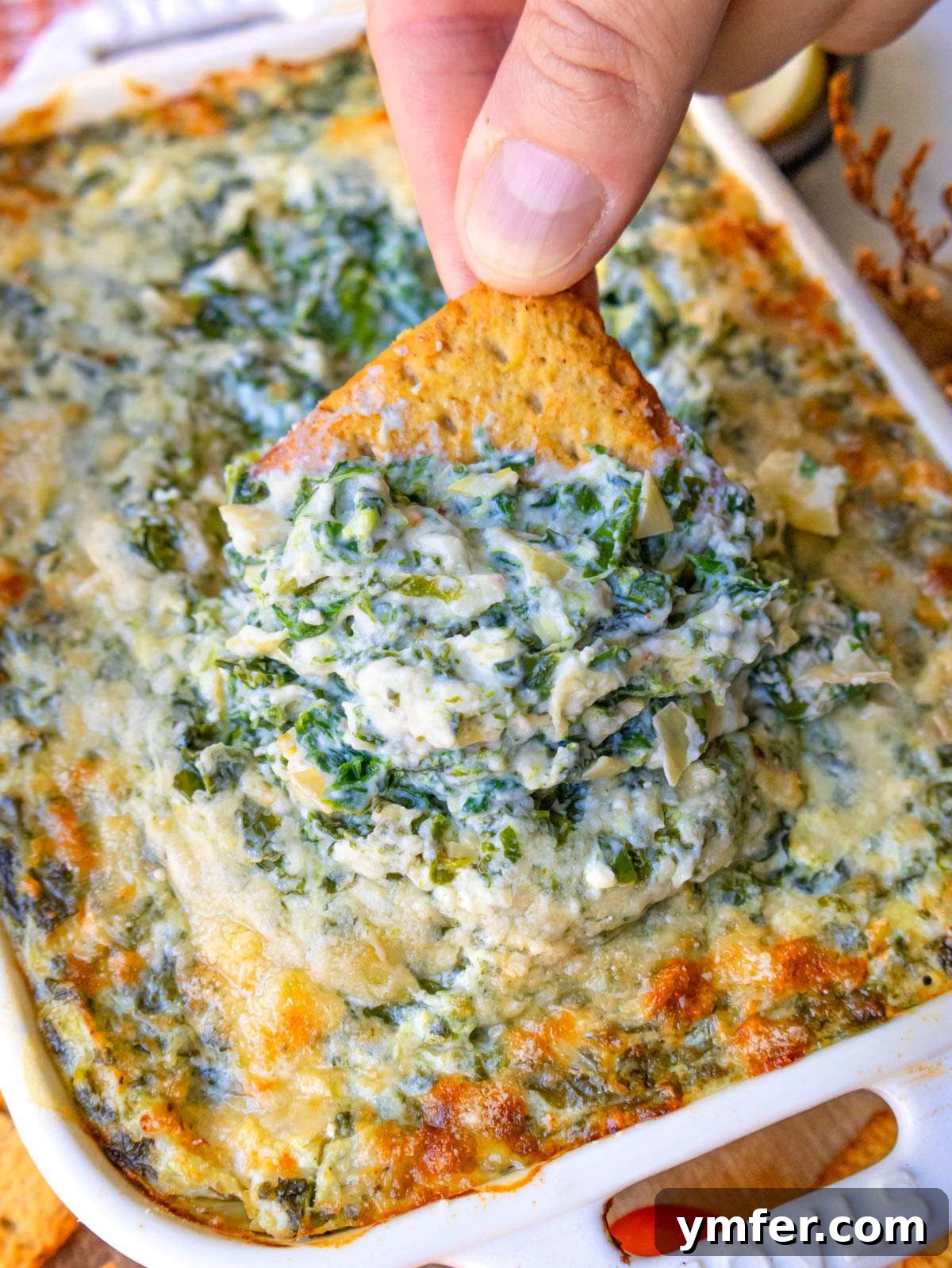 Finished dip close up showing creamy spinach artichoke texture on a cracker.