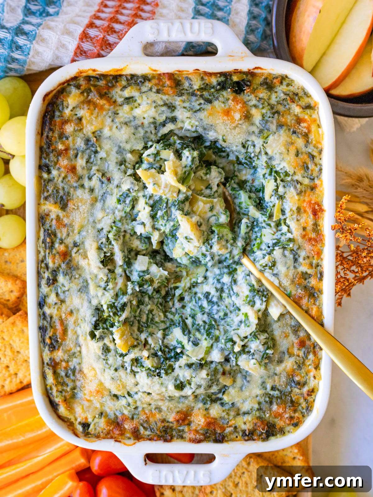 Finished dip top down with golden parmesan crust spoon in and crackers and veggies on the side.