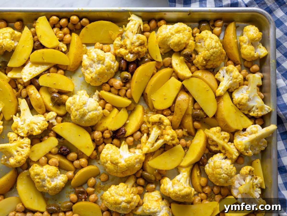 Golden Turmeric Cauliflower and Chickpea Sheet Pan Dinner 6 Step two tossing cauliflower potatoes chickpeas and olives with marinade on sheet pan.