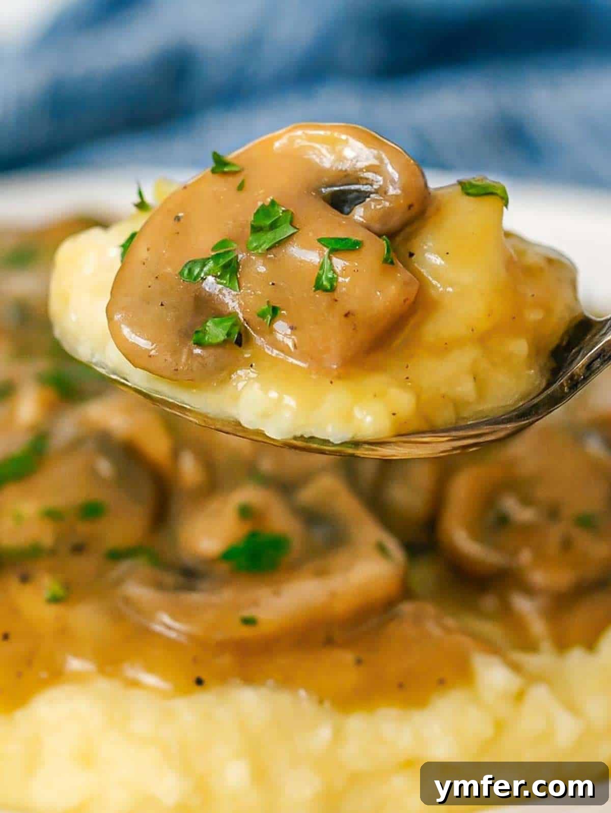 Creamy mushroom sauce, rich and brown, generously drizzled over a spoonful of fluffy mashed potatoes, highlighting its appealing consistency.