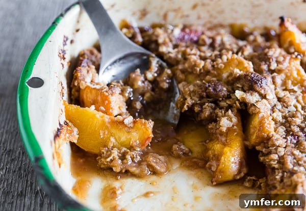 Zesty Ginger Peach Crisp 3 Close-up of ginger peach crisp in a metal baking dish with a spoon, highlighting the crispy topping and soft fruit.