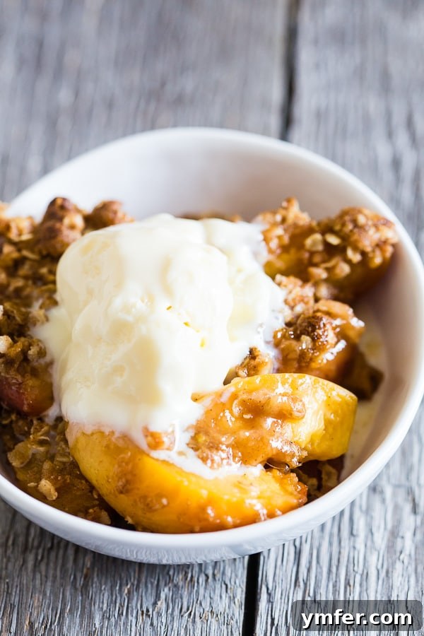 Zesty Ginger Peach Crisp 4 A serving of ginger peach crisp in a white bowl, generously topped with a scoop of vanilla ice cream, ready to be eaten.