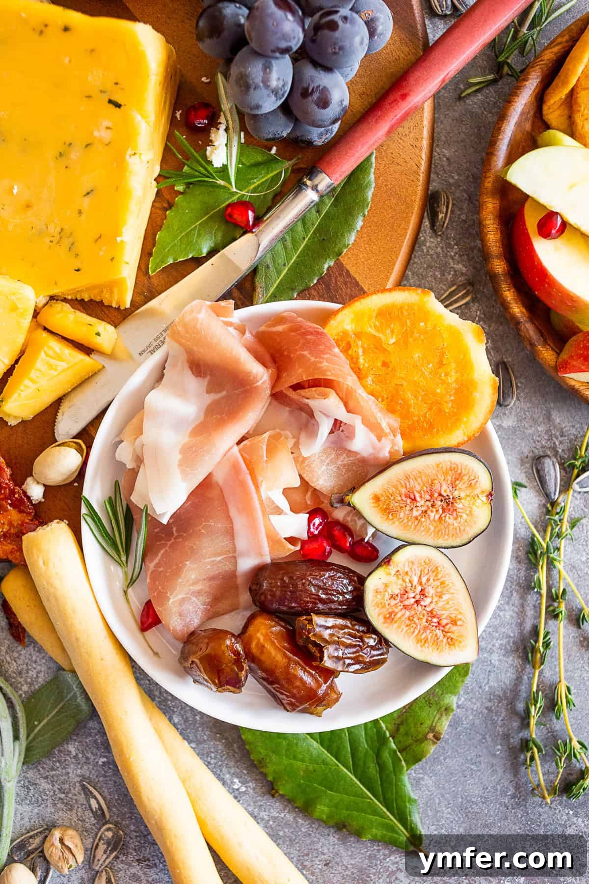 Prosciutto, figs, and dates on a small plate, part of a fall cheese board arrangement.