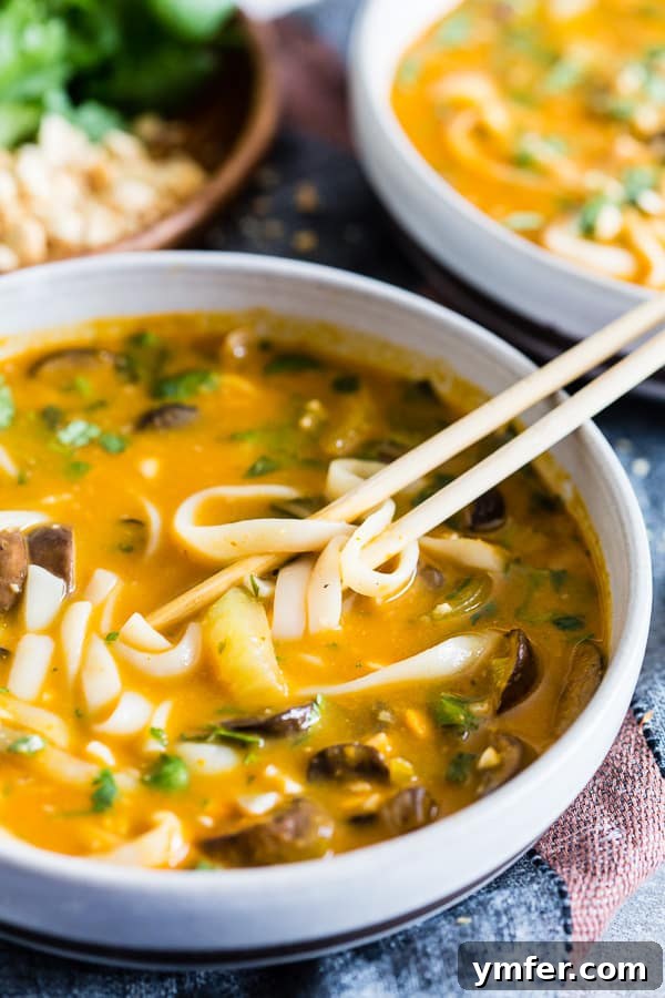 Warming Vegan Pumpkin Red Curry Noodle Soup 5 A single bowl of Vegan Red Curry Pumpkin Noodle Soup with chopsticks resting on the rim, showcasing the noodles and vibrant broth.