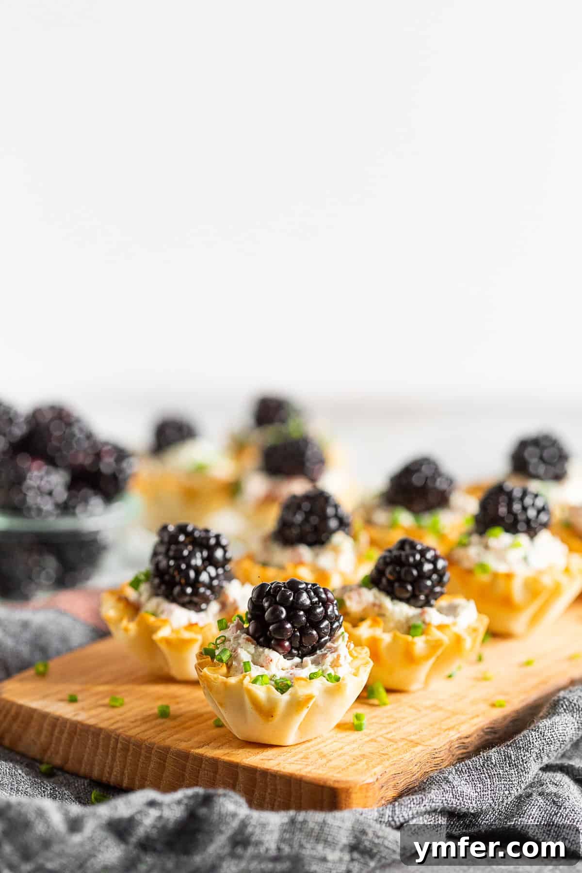 Golden Phyllo Goat Cheese Prosciutto Parcels 3 Close-up shot of Goat Cheese Prosciutto Phyllo Bites, each topped with a single ripe blackberry, highlighting the creamy filling.
