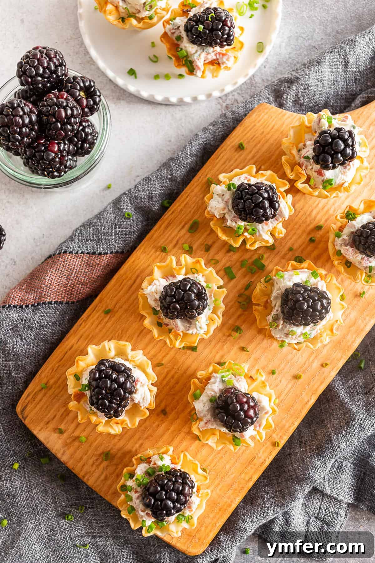 Golden Phyllo Goat Cheese Prosciutto Parcels 5 A close-up of Goat Cheese Prosciutto Phyllo Bites arranged elegantly on a white serving board with sprigs of rosemary for garnish.