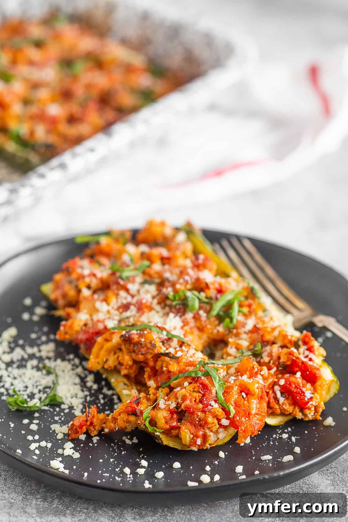 Cheesy Chicken Parm Zucchini Boats 2 Ground Chicken Parmesan Stuffed Zucchini Boats on a plate, ready to be enjoyed. Highlighted ingredients include ground chicken, fresh basil, Italian seasoning, diced tomatoes, and mozzarella cheese.
