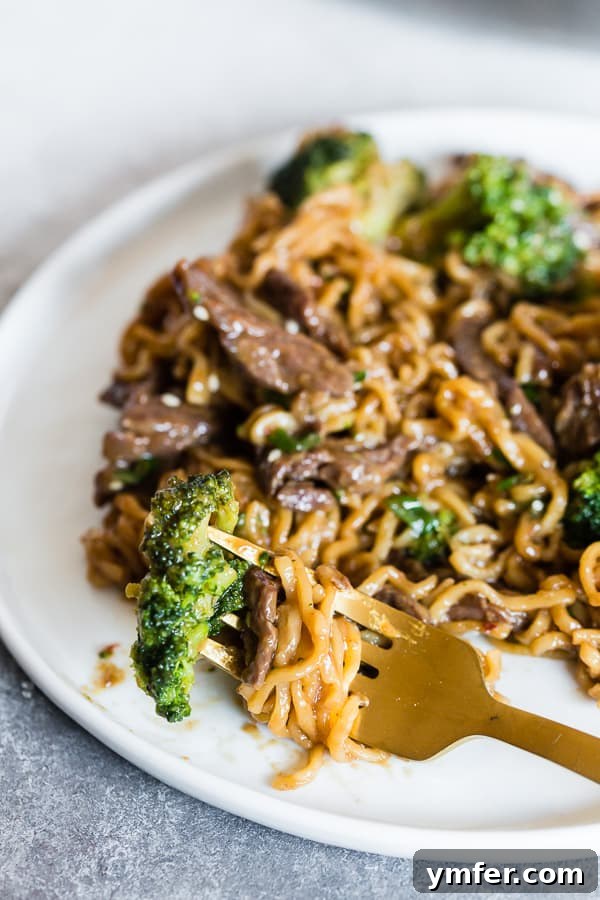Close-up of Beef and Broccoli Ramen Noodles on a white plate, with a fork digging in.