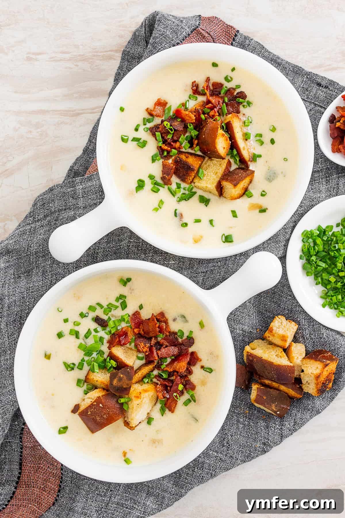 Champion Beer Cheese Soup 2 Two white bowls of Beer Cheese Soup, generously topped with crispy bacon, golden pretzel croutons, and fresh green chives, ready to be enjoyed.