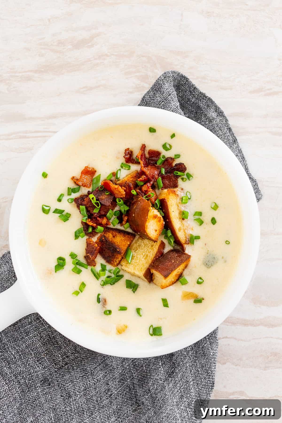 Champion Beer Cheese Soup 5 A top-down view of Beer Cheese Soup in a bowl, artfully topped with golden pretzel croutons, finely chopped green chives, and bits of crispy bacon.