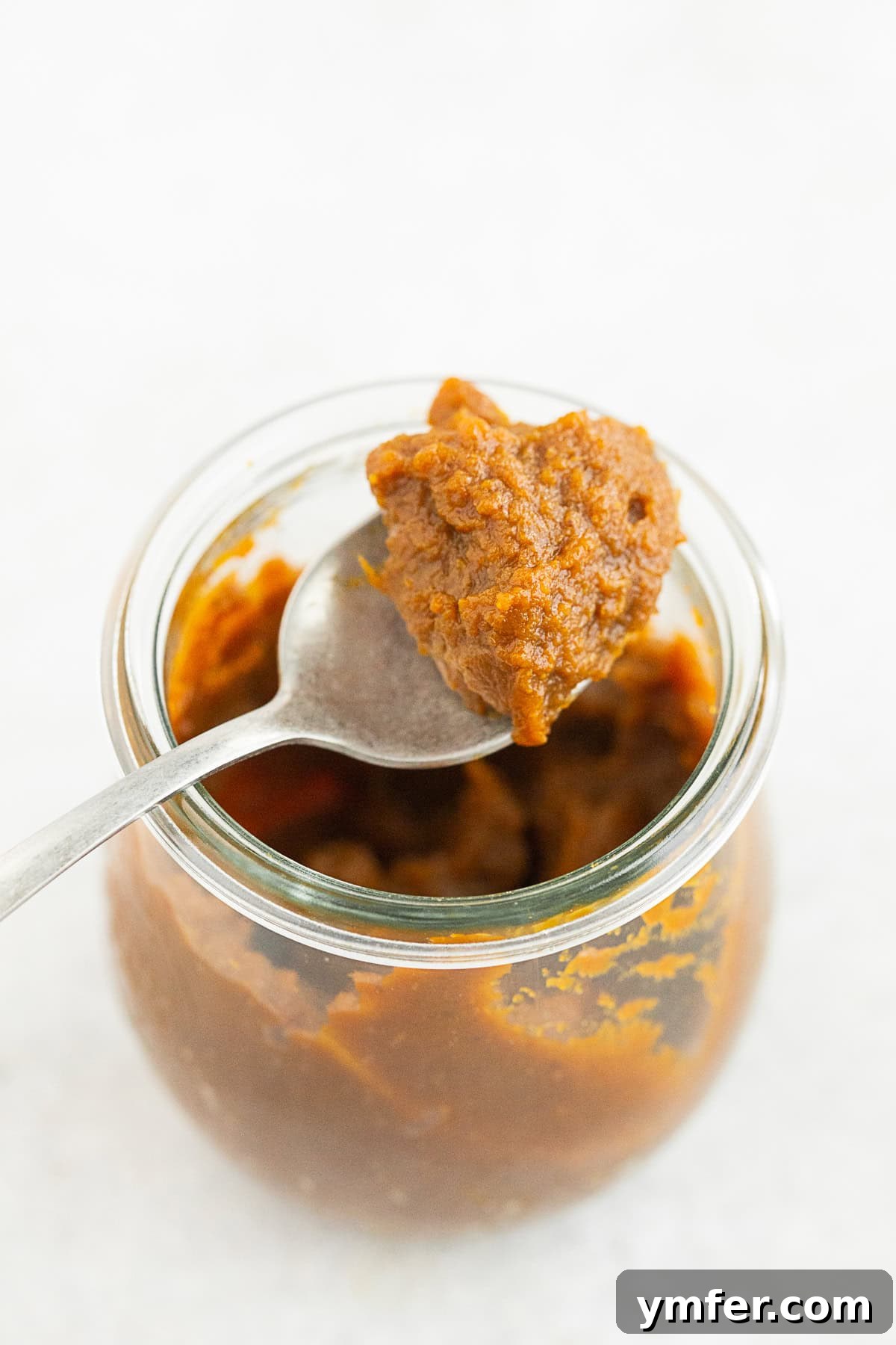 Ultimate Apple Butter Recipes 3 A glass jar filled with rich, homemade apple butter, next to a spoon, inviting you to discover its deliciousness.