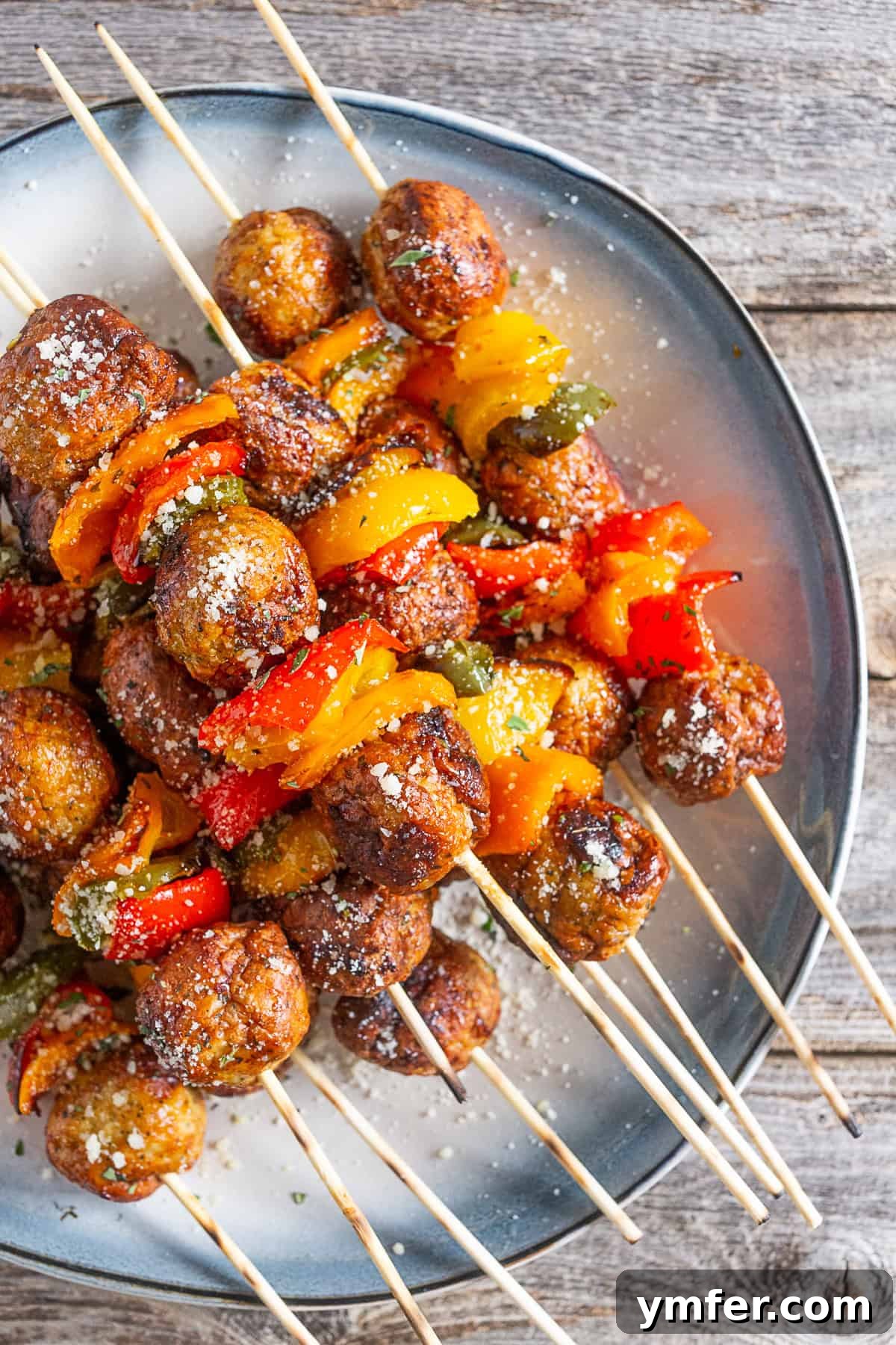 Fire-Kissed Chicken Meatball Skewers 2 Grilled Chicken Meatball Skewers on a plate, garnished with fresh herbs and Parmesan.