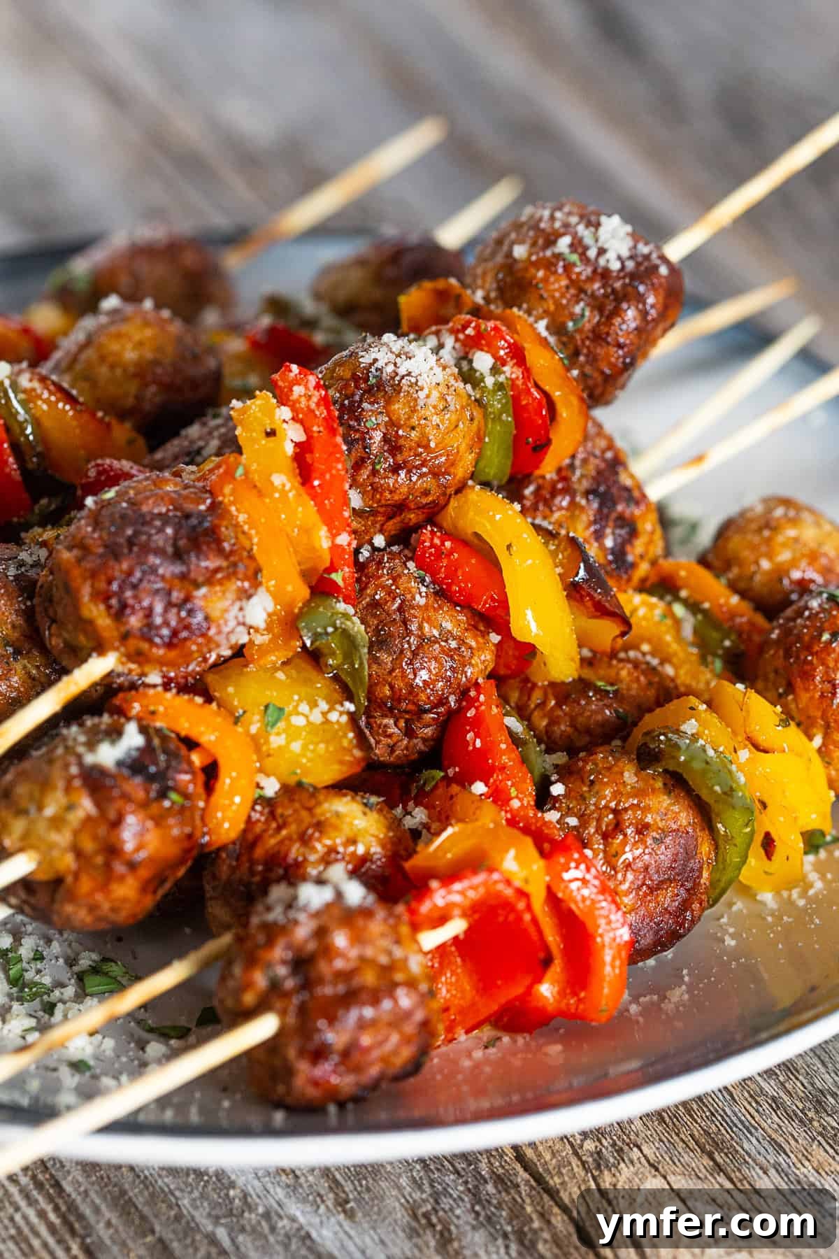 Fire-Kissed Chicken Meatball Skewers 4 Grilled Chicken Meatball Skewers on a plate sprinkled with Parmesan cheese, ready to be served.