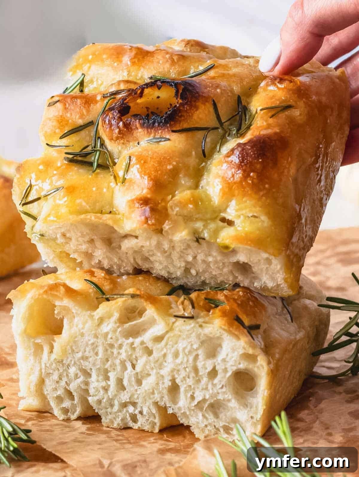 Golden Focaccia Perfection 2 Two golden-brown pieces of homemade focaccia, one resting atop the other, adorned with fresh rosemary and flaky sea salt.