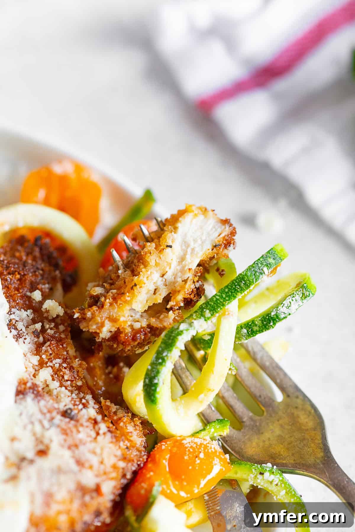 Summertime Zucchini Noodle Chicken Parm 4 A fork taking a bite of Summer Chicken Parmesan with Zoodles, showing the crispy chicken and fresh noodles.