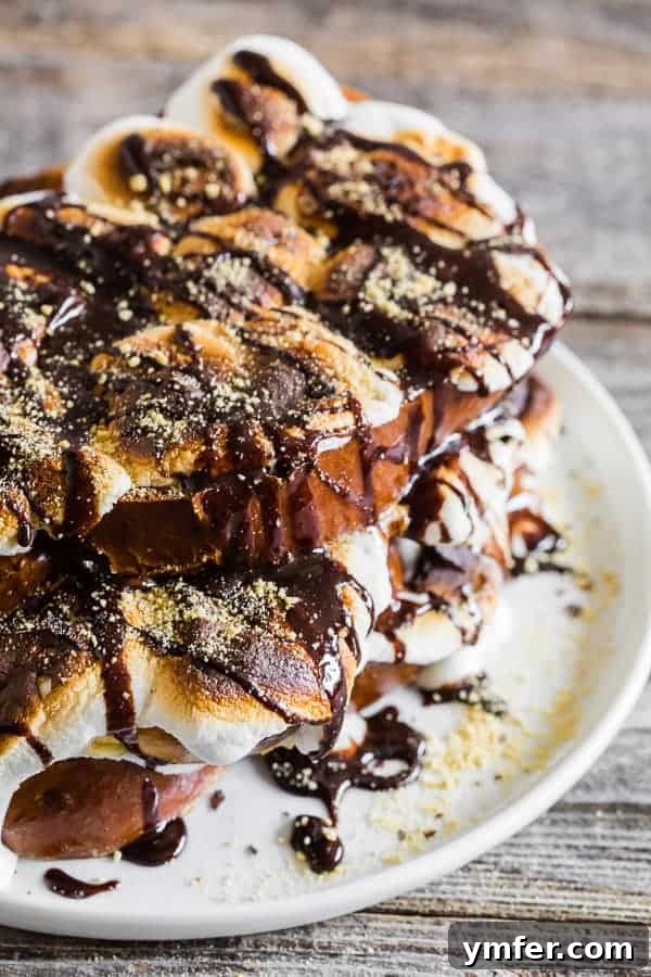 Gooey Smores French Toast 2 S'mores French toast served on a white plate with chocolate sauce drizzled on top, showcasing golden-brown bread and perfectly toasted marshmallows.