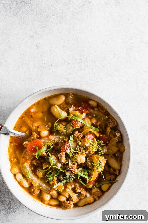 Italian Sausage Fennel White Bean Soup served in a white bowl with fresh basil.