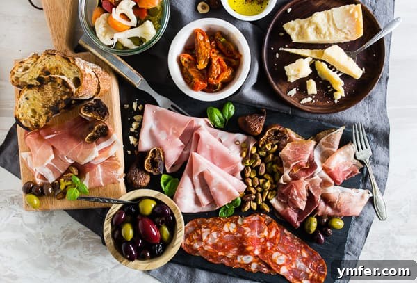 Overhead view of Italian charcuterie board with meats, cheese, olives, nuts, bread and tomatoes.