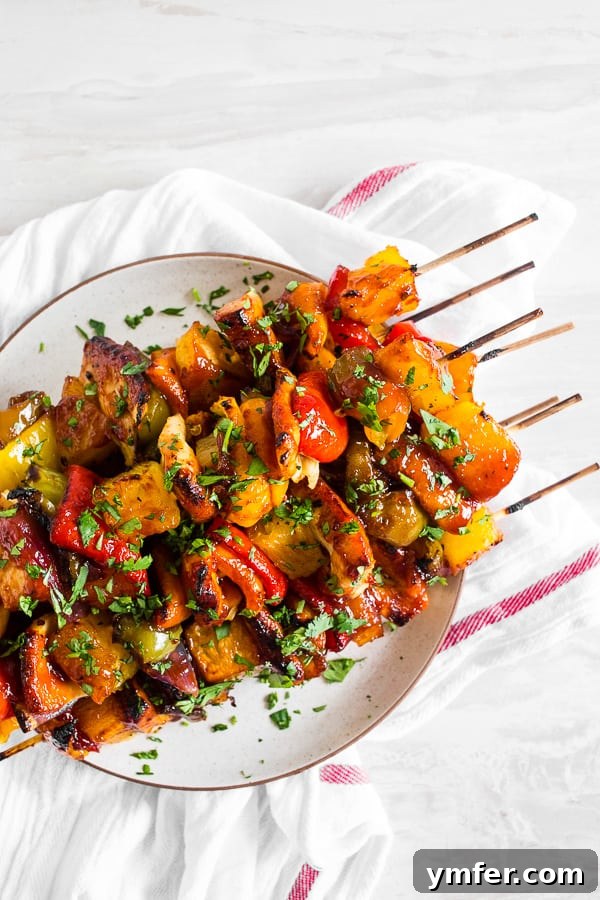 Island Pineapple Chicken Skewers 4 Freshly grilled Pineapple Chicken Kebabs garnished with minced parsley on a white platter.
