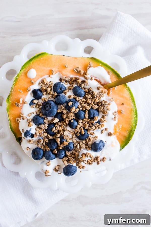 A refreshing Crunchy Yogurt Cantaloupe Breakfast Bowl, perfectly portioned in half a cantaloupe, topped with creamy yogurt, fresh blueberries, and crispy Grape Nuts cereal.
