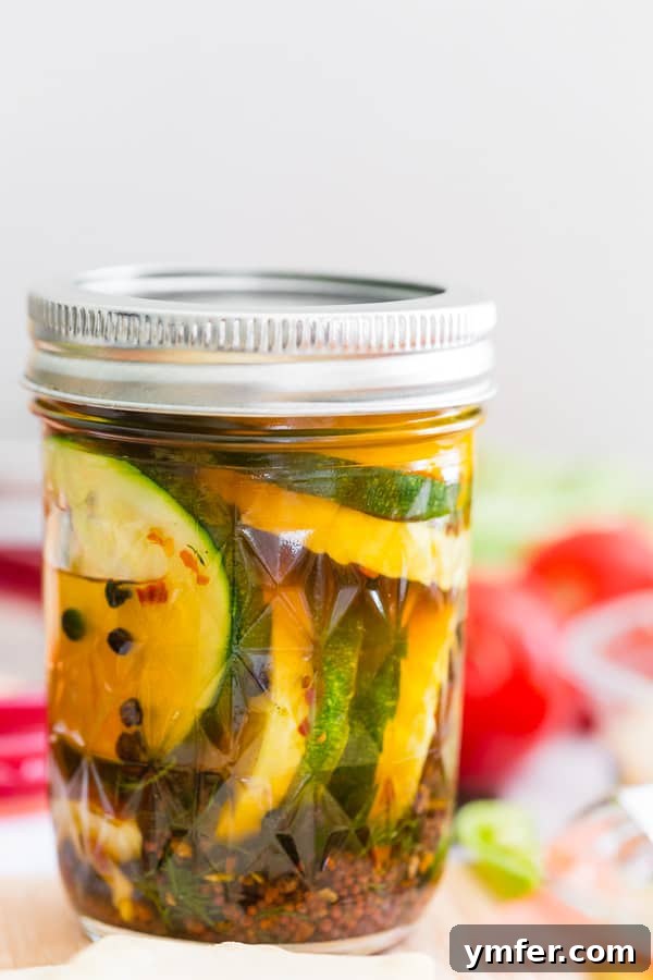 Zesty Zucchini Zingers 2 Sweet and spicy zucchini pickles in a clear glass canning jar, showcasing the vibrant green and yellow slices along with spices like dill and red pepper flakes.