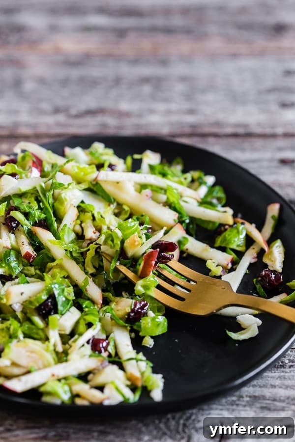 Zesty Apple & Brussels Slaw 3 A fork grabbing a perfect bite of Tangy Brussels Sprout Apple Slaw, highlighting the shaved sprouts, apple matchsticks, and cranberries.