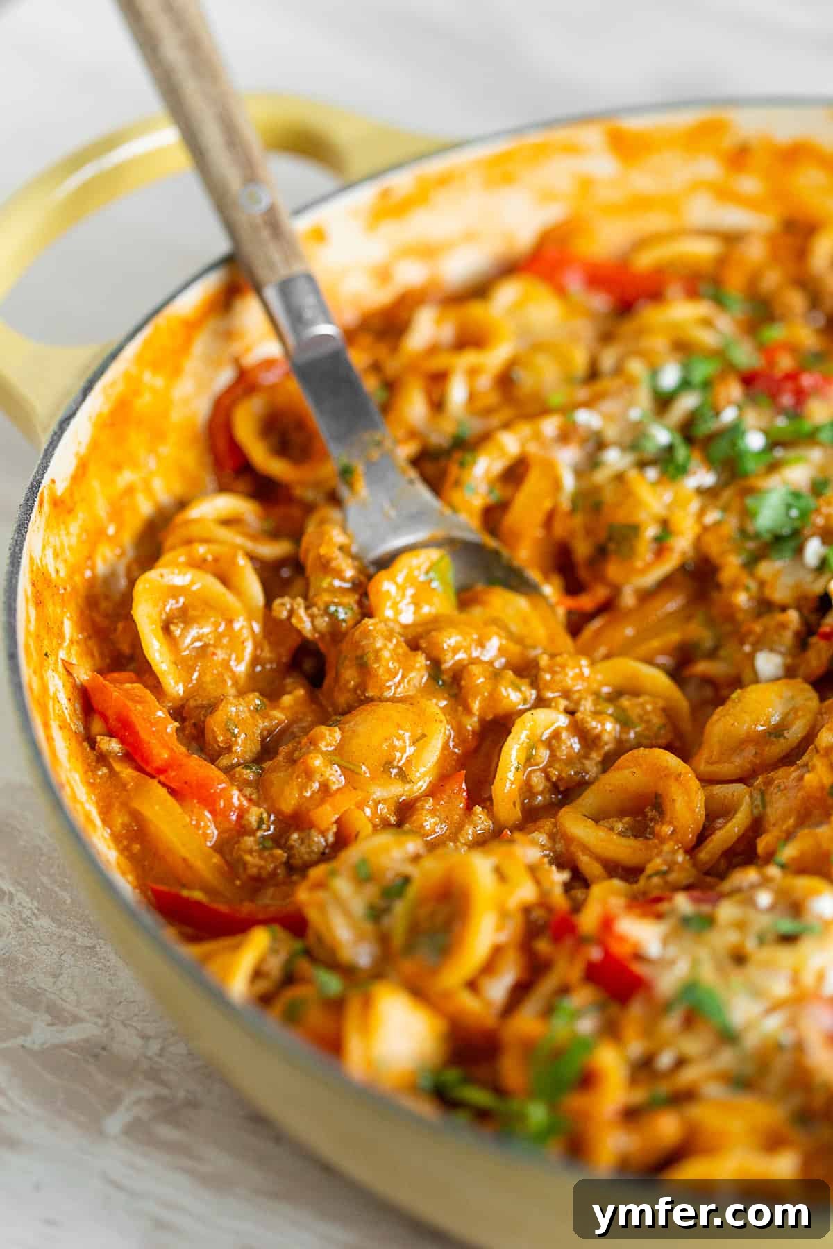 Zesty One-Pot Ground Chicken Fajita Pasta 4 A close-up of One-Pot Ground Chicken Fajita Pasta in a yellow dish with a spoon, showing its creamy texture.