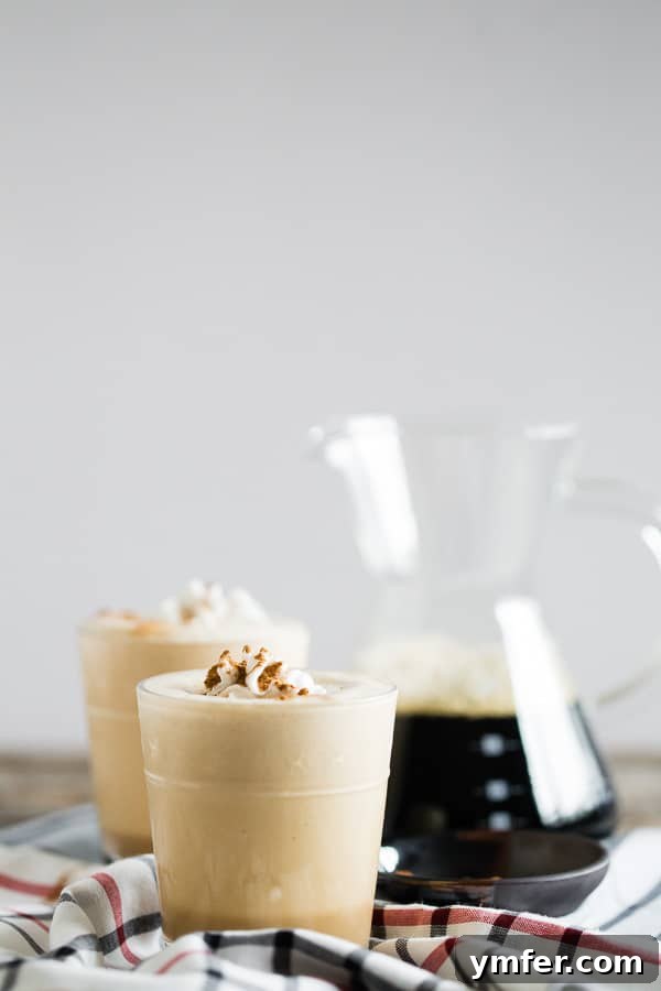 Pumpkin Spice Power Brew 4 A Pumpkin Spice Coffee Protein Shake in a glass, topped with whipped cream and a sprinkle of spice, accompanied by a jug of iced coffee.