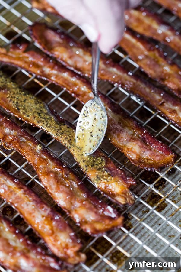A spoon meticulously applying a generous amount of pepper sauce onto a piece of cooked bacon.