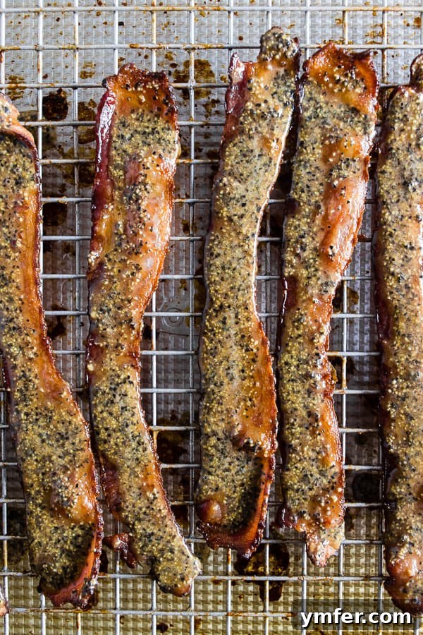 Strips of Maple Black Pepper Bacon, beautifully slathered in the sweet and spicy dressing, laid out on a sheet pan, waiting to be cooked to perfection.