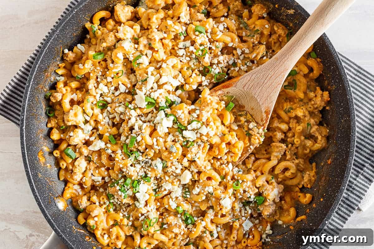 Creamy One Pot Buffalo Chicken Pasta 7 One Pot Buffalo Chicken Pasta in a skillet, with a wooden spoon ready to serve.