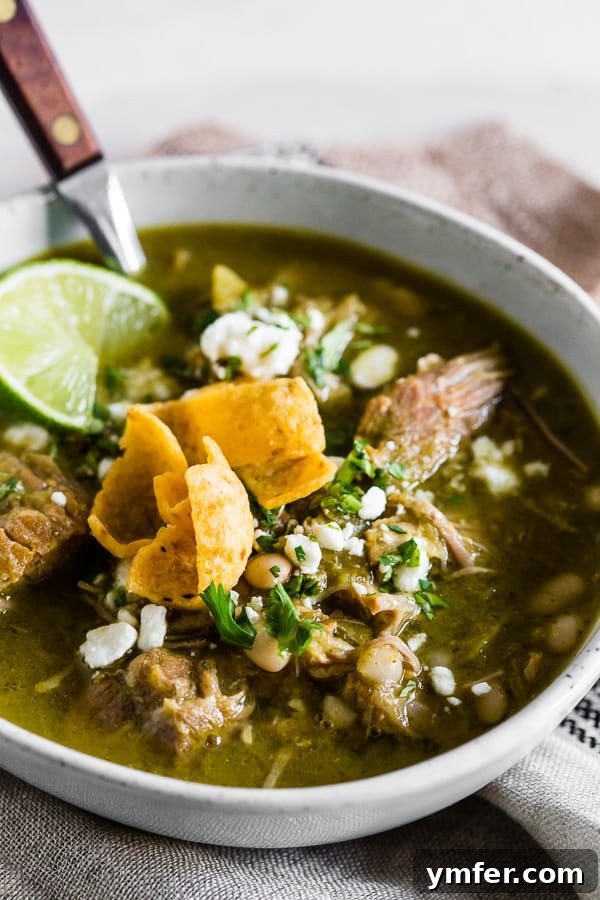 Zesty Instant Pot Pork Chili Verde 2 A steaming bowl of Instant Pot Pork Chili Verde, garnished with fresh cilantro and a sprinkle of Cotija cheese. The chili is rich green, with visible chunks of pork and beans.