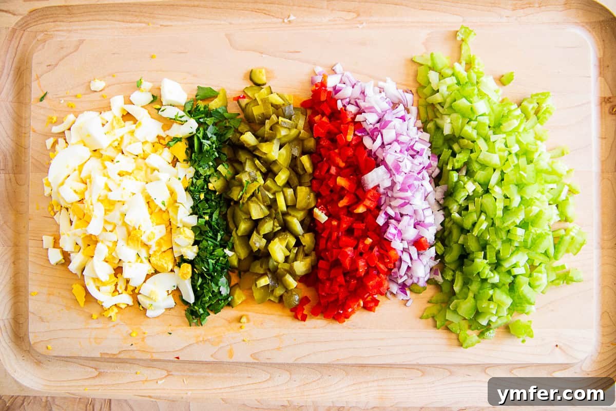 Grandma's Macaroni Salad 3 Finely chopped celery, red onion, red bell pepper, pickles, parsley, and hard-boiled eggs on a cutting board, prepared for mixing.