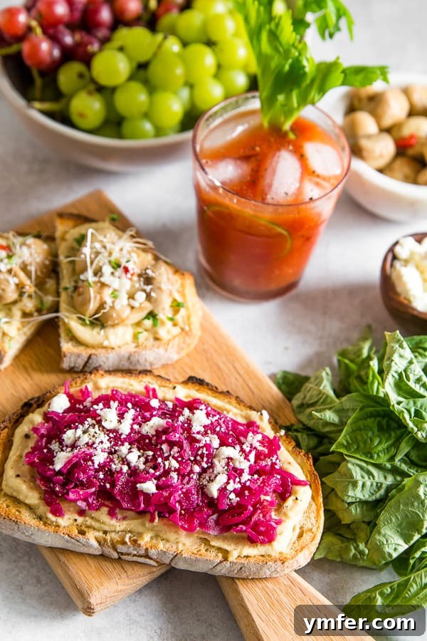 A Horseradish Bloody Mary cocktail alongside a selection of hummus toasts on a wooden tray, ready for serving.