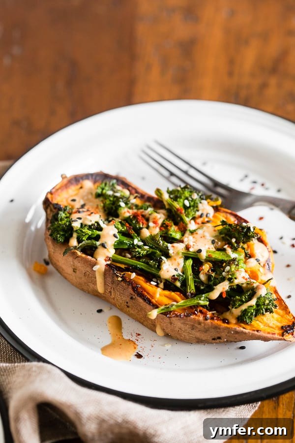 Loaded Sweet Potatoes with Broccoli Rabe and Hummus 4 A single baked sweet potato half, generously topped with roasted broccoli rabe and a smooth hummus drizzle, resting on a white plate.