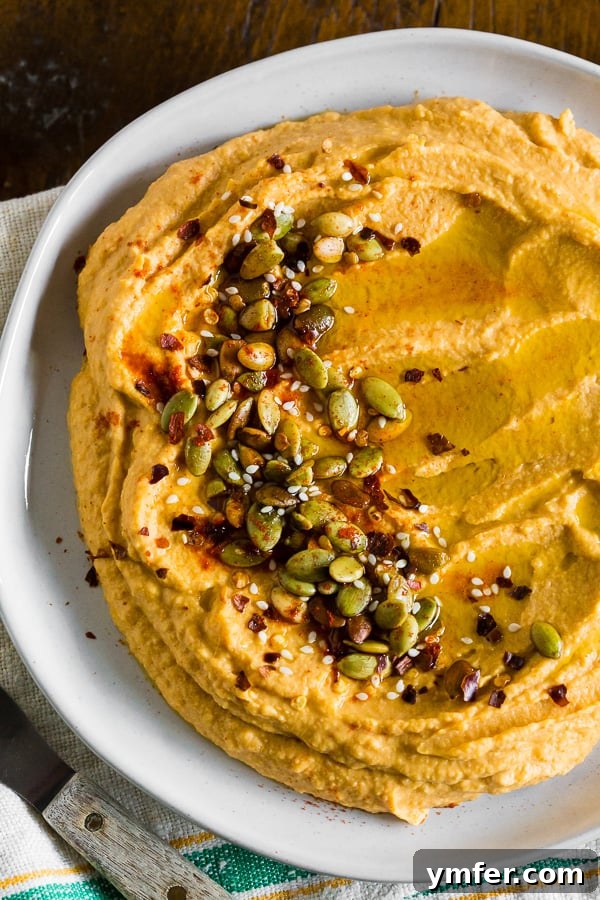 Quick Autumn Pumpkin Hummus 2 Close-up of creamy pumpkin hummus garnished with pumpkin seeds and a drizzle of olive oil.
