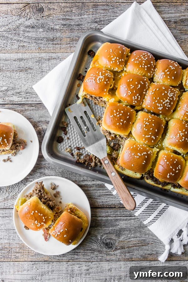 Cheesy Bacon Pull-Apart Sliders 2 A tray full of golden brown baked bacon cheeseburger sliders, with a few on a serving plate, ready to be enjoyed.